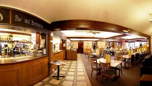 Een bar en brasserie met een geruit vloertje, houten meubels en een plafondventilator.