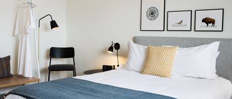 A neatly arranged hotel room with a bed, a chair, a bedside table with a lamp, and framed pictures on the wall.