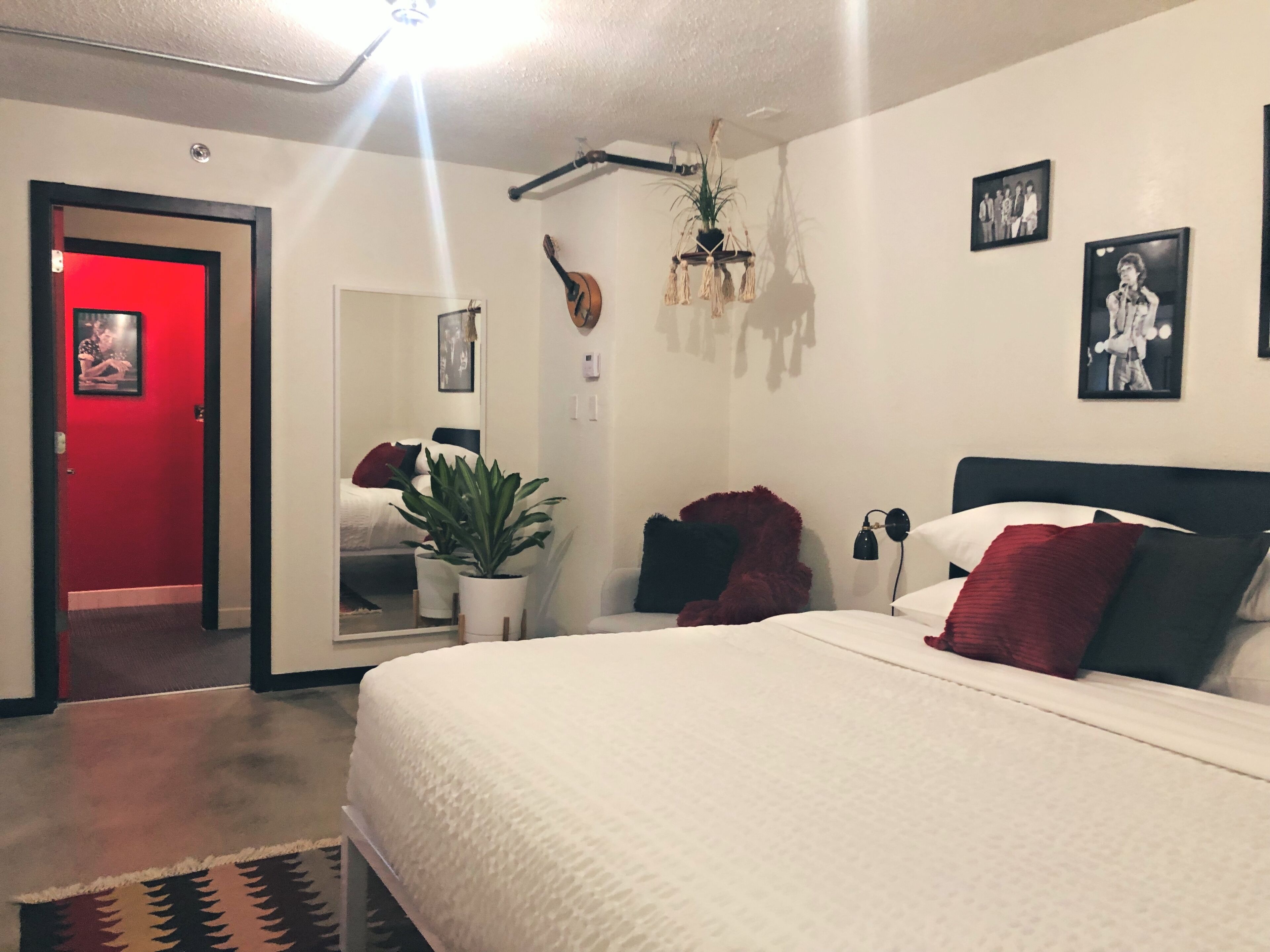 Ein Schlafzimmer mit einem großen Bett, einer roten Tür, einem Blumentopf und einer Chandelier.