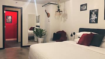 A bedroom with a large bed, a red door, a potted plant, and a chandelier.