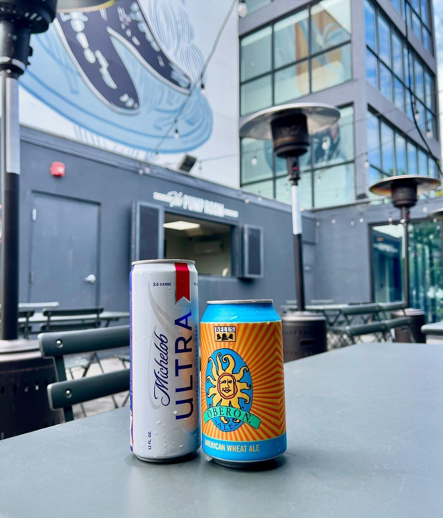Dos latas de cerveza sobre una mesa con un edificio moderno al fondo.