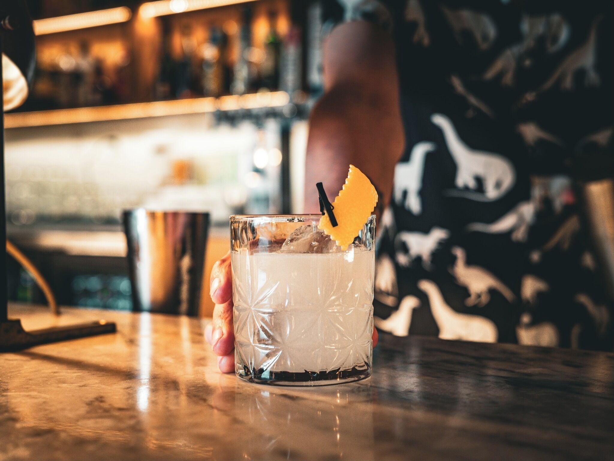 A glass of a clear beverage with ice cubes and a garnish, placed on a bar counter.