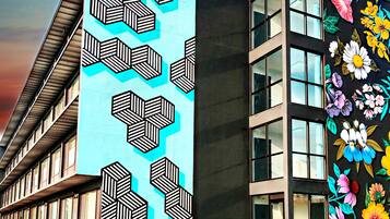 A modern building with a geometric pattern mural on one side and a colorful floral mural on the other.