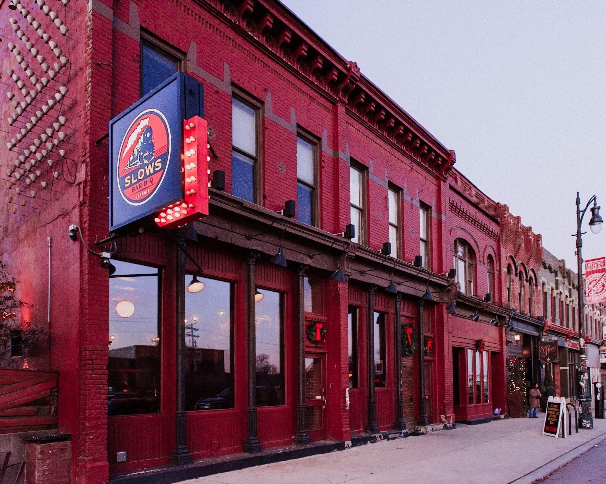 A red brick building with a 'SLOWS BAR B Q' sign, large windows, and a sidewalk with a signboard.
