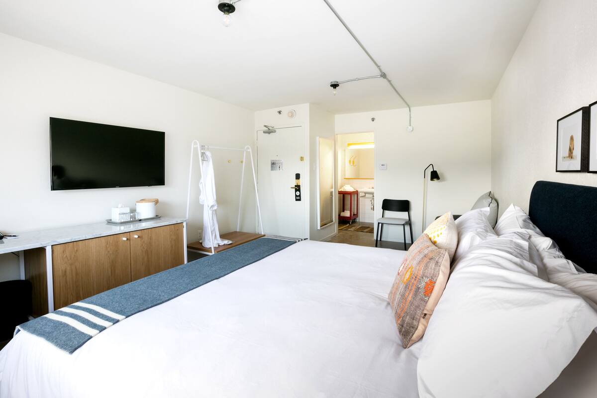 A modern hotel room with a large bed, a flat-screen TV, a wooden desk, and a shower area.