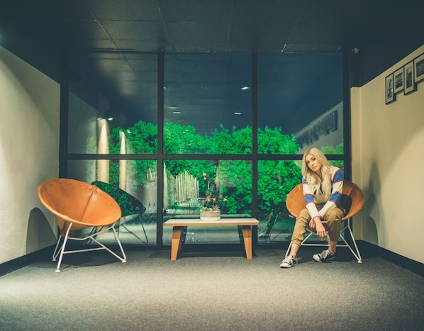 A room with large windows, a table, two chairs, and a person sitting on one of the chairs.