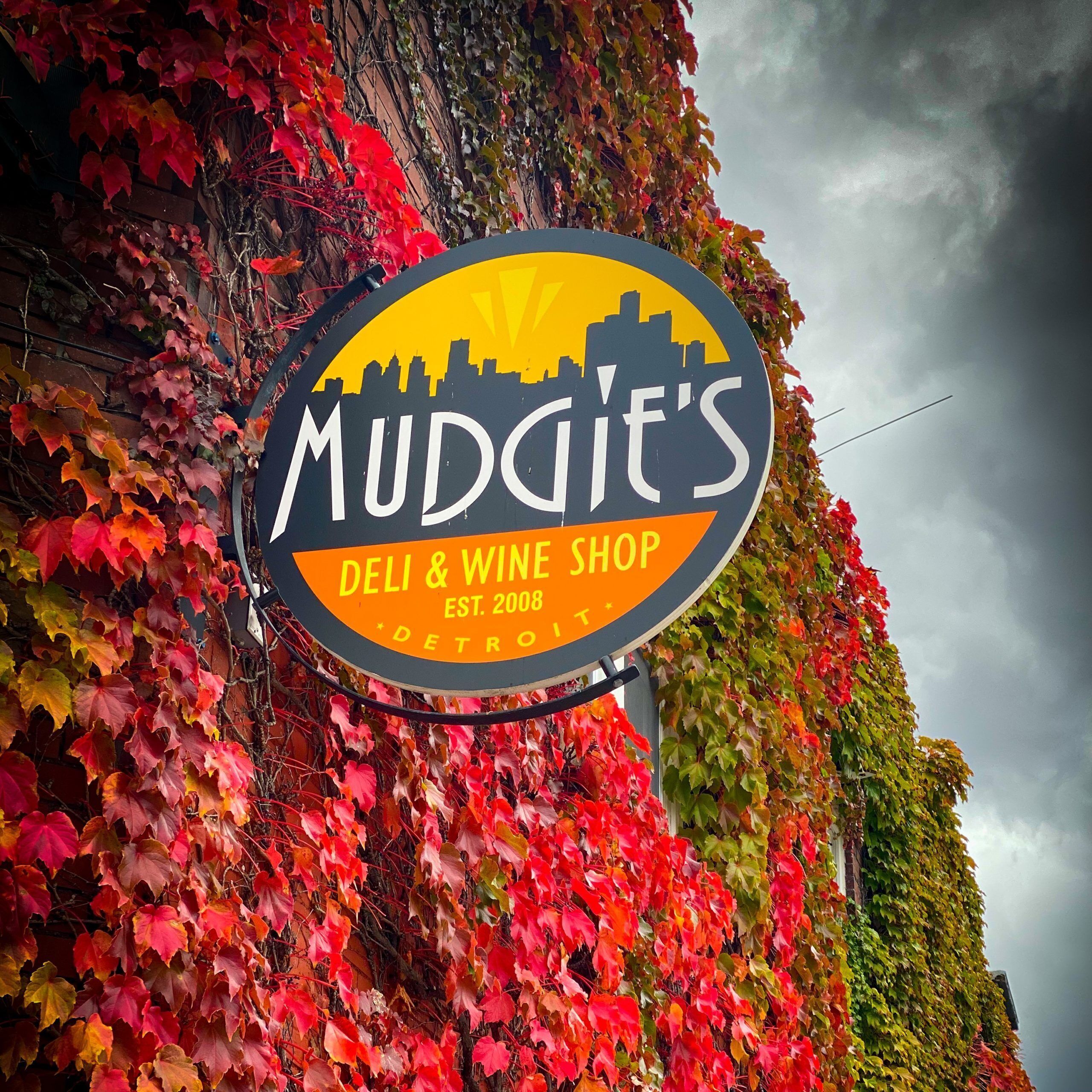 A sign for MUDGIT'S DELI & WINE SHOP with a city skyline silhouette, established in 2008, and located in Detroit.