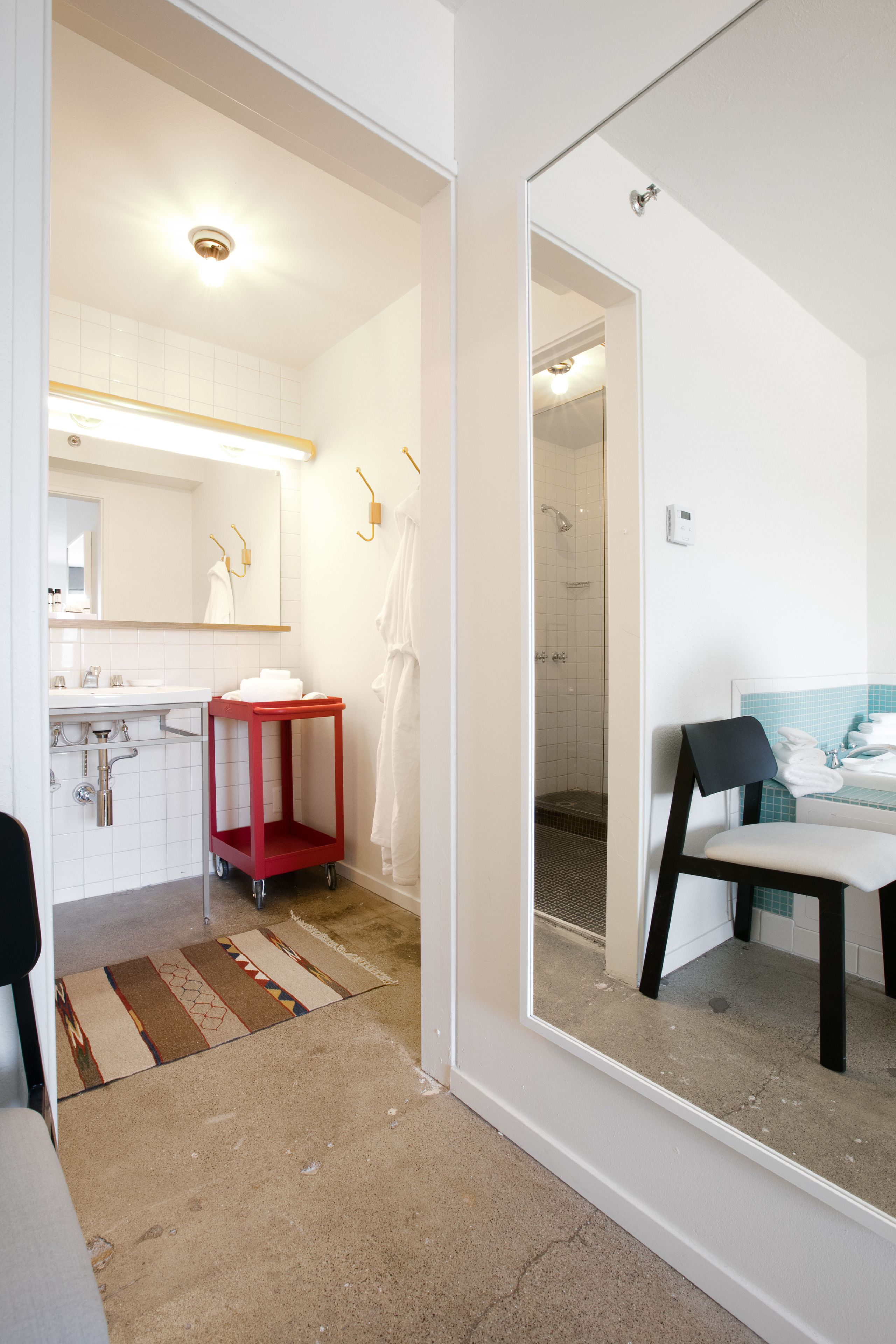 A modern bathroom with a white sink, mirror, and towel rack. There is a red cart and a shower area visible.