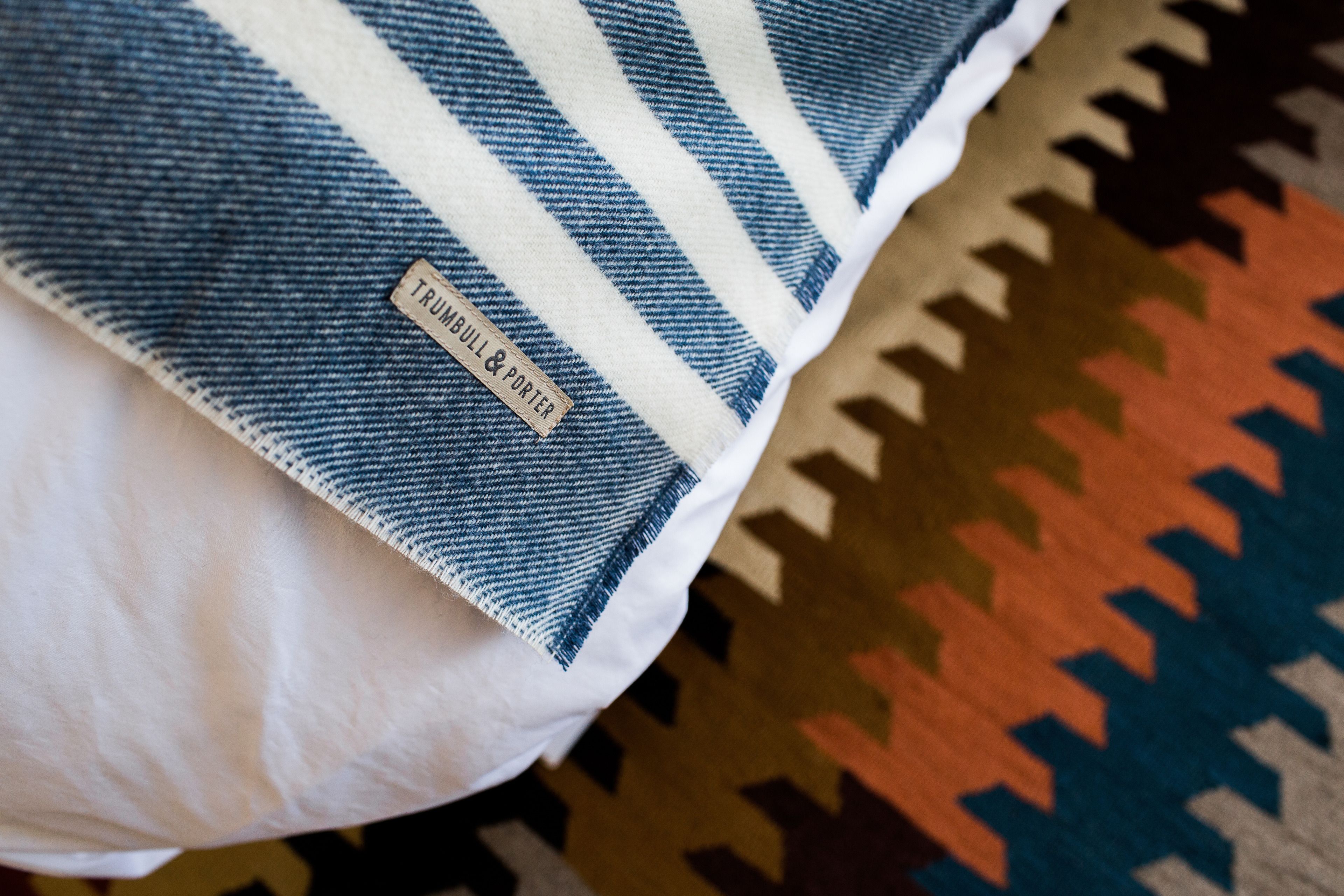 A pillow with a label reading "TRUMBULL & PORTER" on a bed with a patterned bedspread.