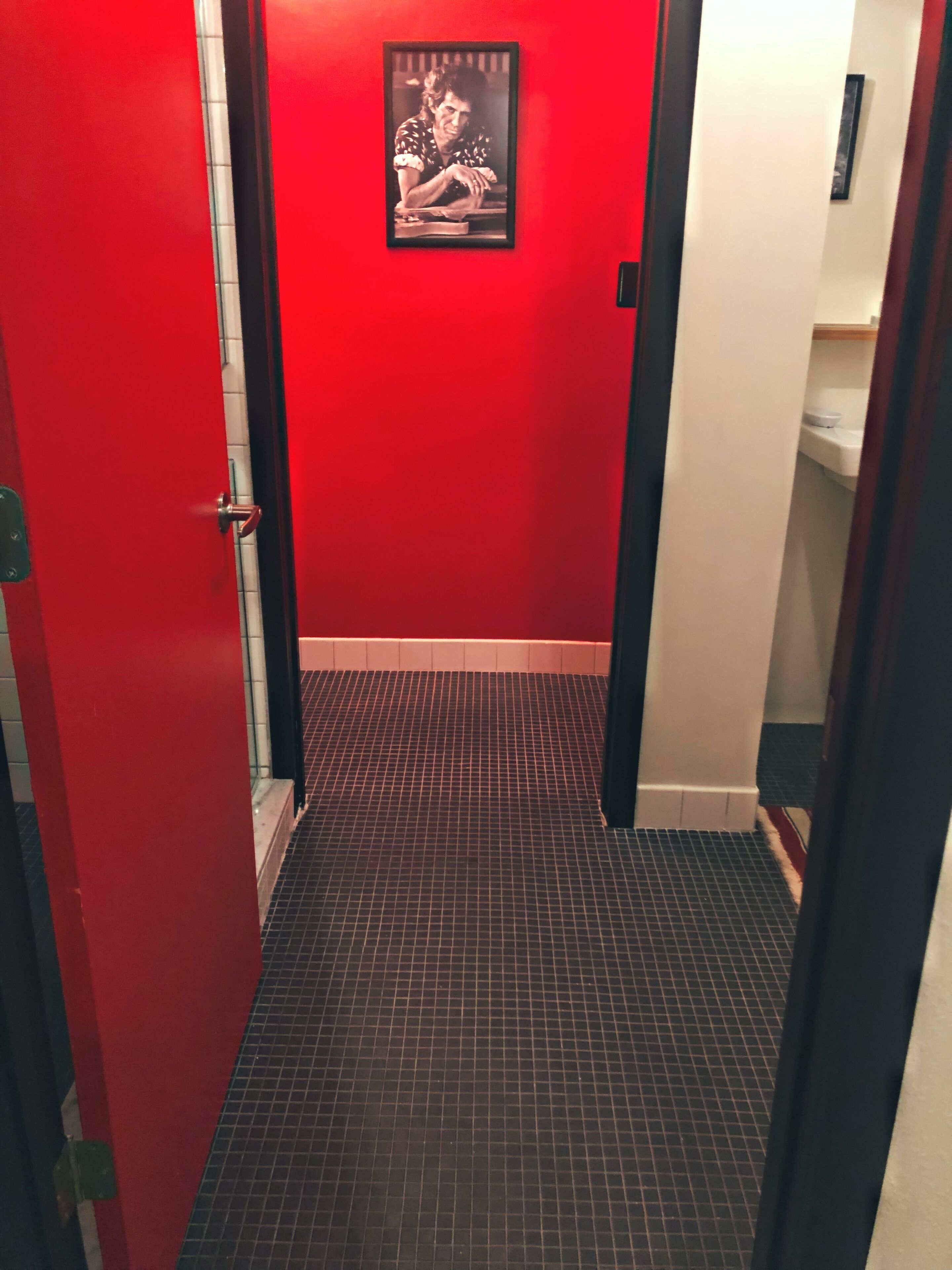 Un pasillo con paredes rojas y suelo de baldosas que conduce a un baño.