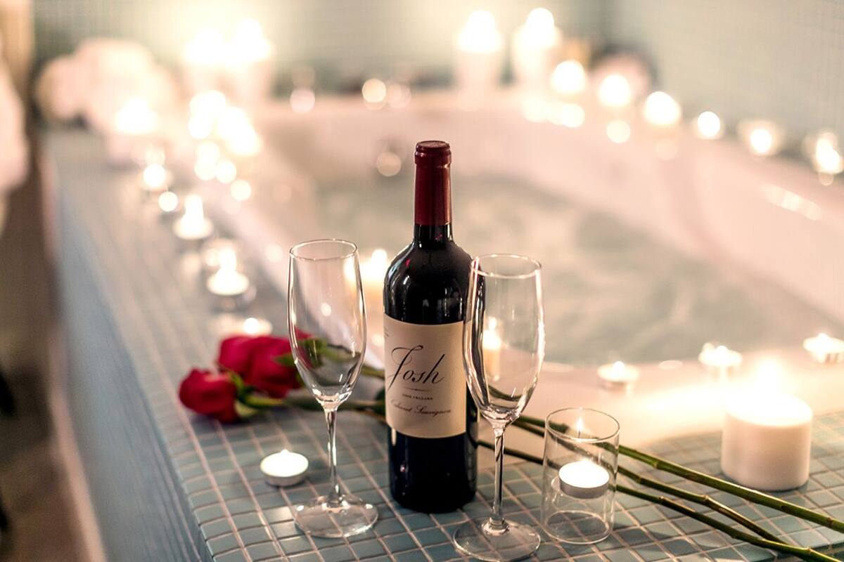 A bottle of wine on a table with two glasses and a rose.