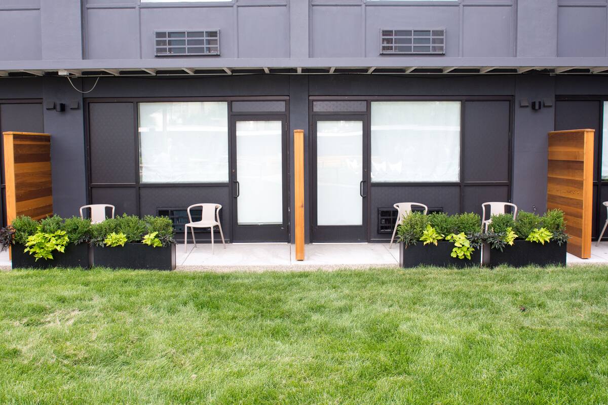 A modern building with a flat roof, large windows, and a front entrance. There are two black doors with glass panels, and a set of white chairs and tables outside.