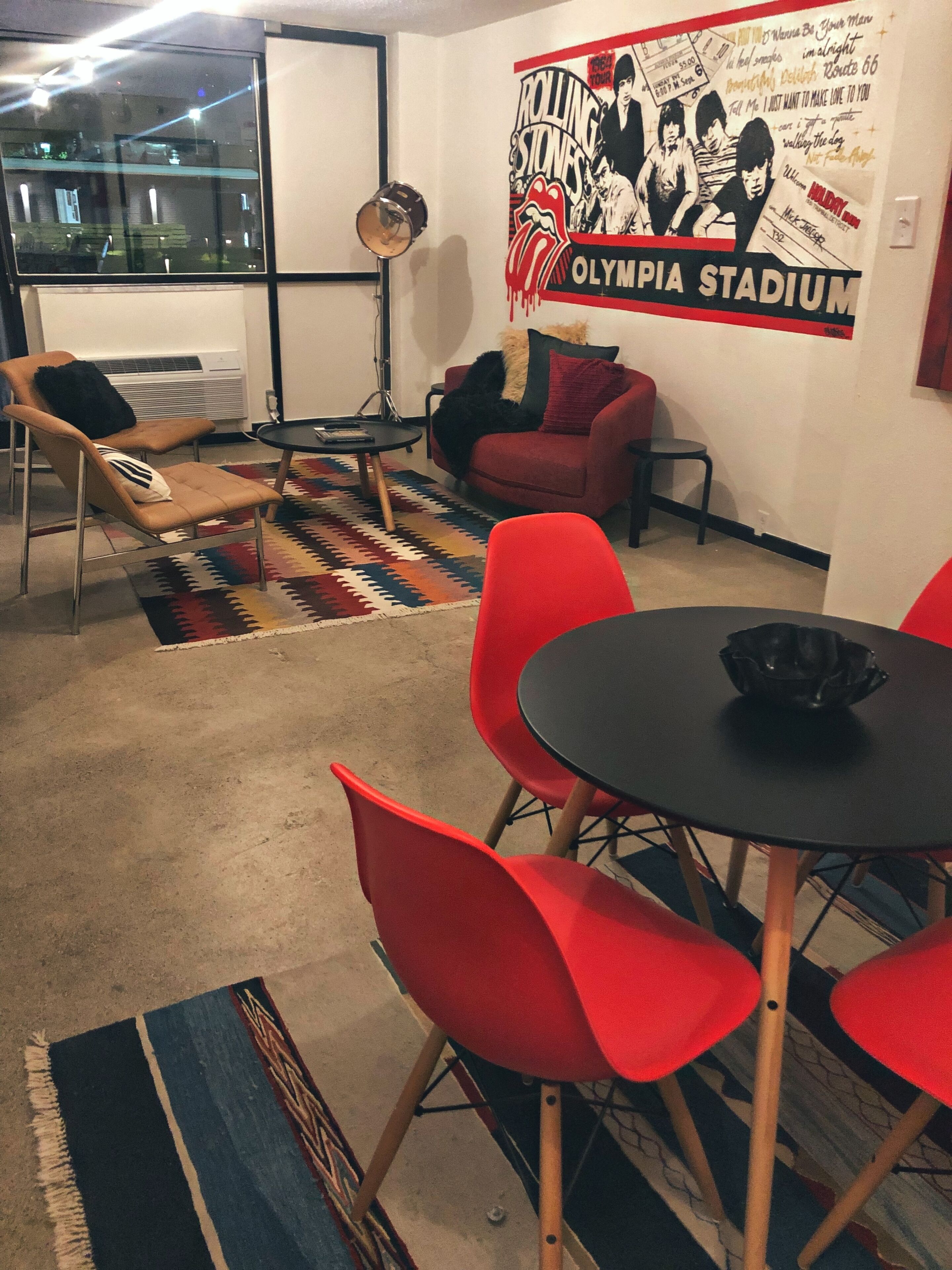 Ein Zimmer mit einem roten Sofa, einem schwarzen Tisch und einem Rolling Stones Poster an der Wand.