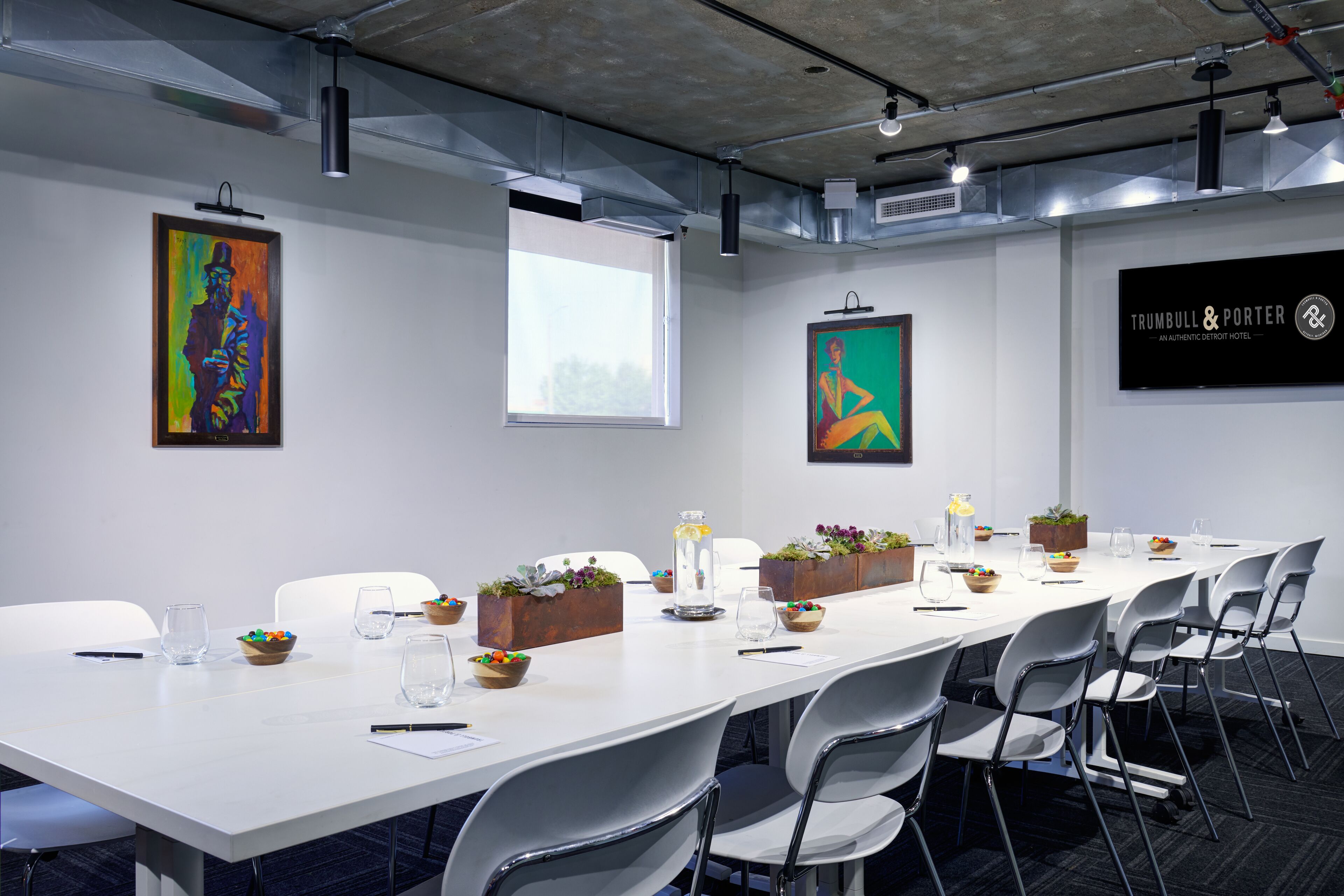 A conference room with a long table, white chairs, and artwork on the walls.