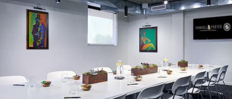 A conference room with a long table, white chairs, and artwork on the walls.