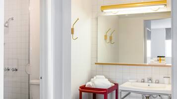 A bathroom with a white toilet, a red cart with towels, a sink, and a mirror.