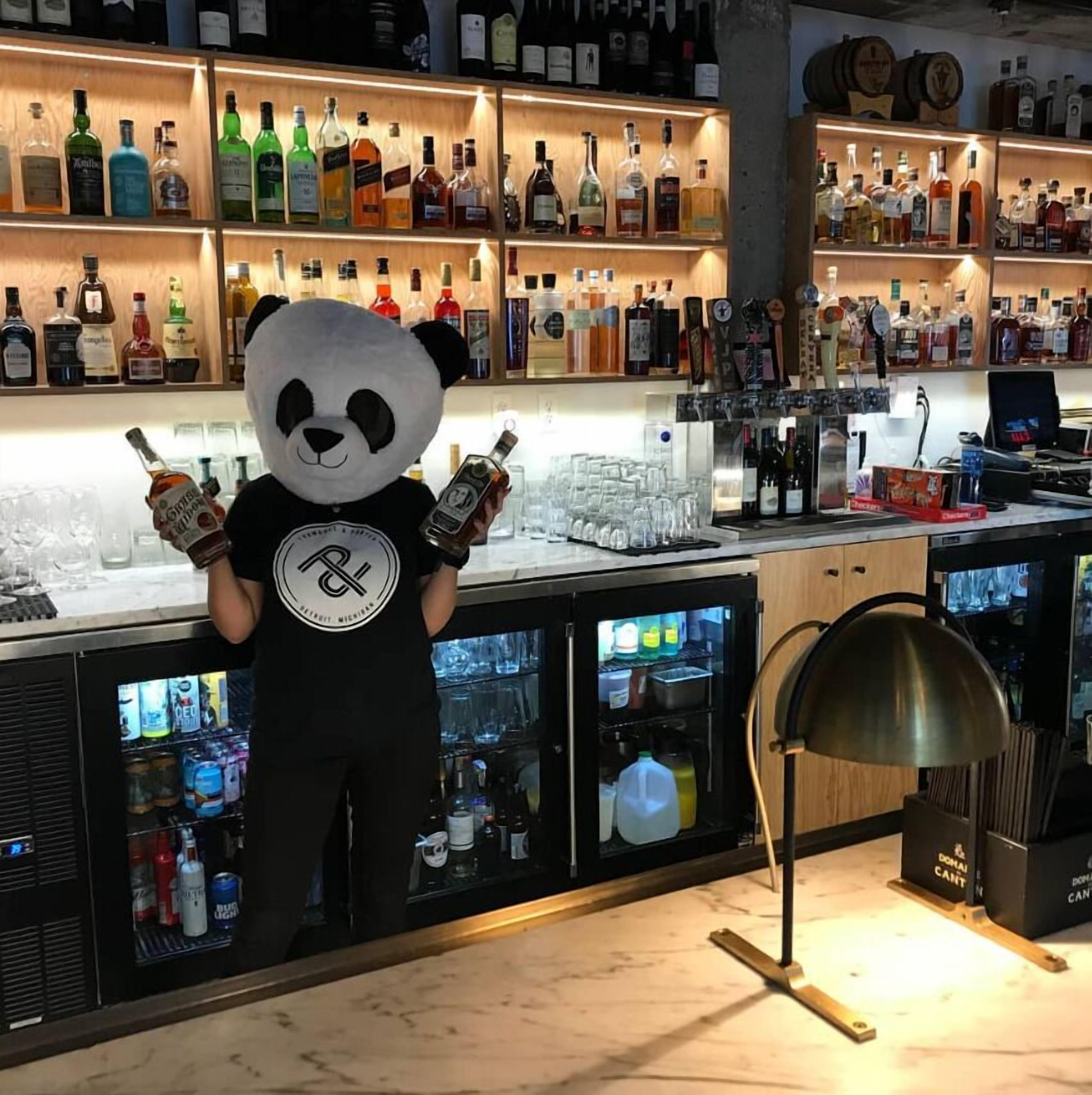 A bar area with shelves of liquor bottles, a panda mascot holding a bottle, and a bar counter with glasses and a cash register.