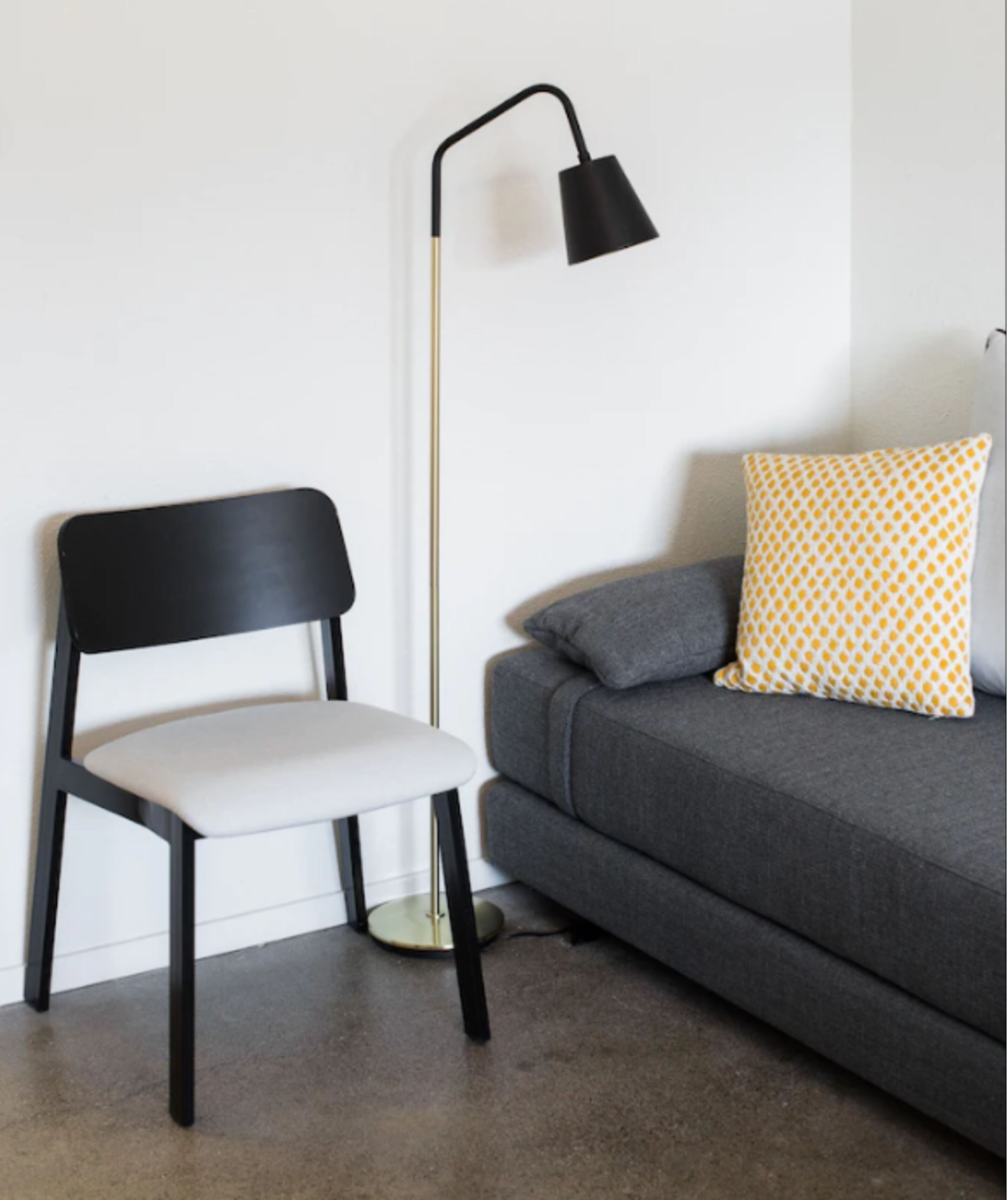A modern room with a black chair, a grey sofa, a patterned pillow, and a floor lamp.