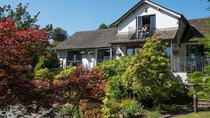 A two-story house with a balcony, surrounded by various trees and shrubs. - Windermere Rooms at The Wateredge Inn (Ambleside)