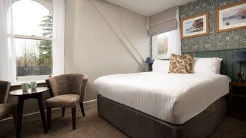 Une chambre à coucher avec un grand lit, deux chaises, une petite table et une fenêtre avec des rideaux.