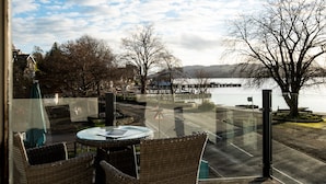 A view from a balcony with wicker chairs and a table, overlooking a body of water and a bridge. - Windermere Rooms at The Wateredge Inn (Ambleside)