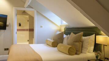 Una habitación de hotel con cama, almohadas, mesita de noche, lámpara y televisor en la pared.