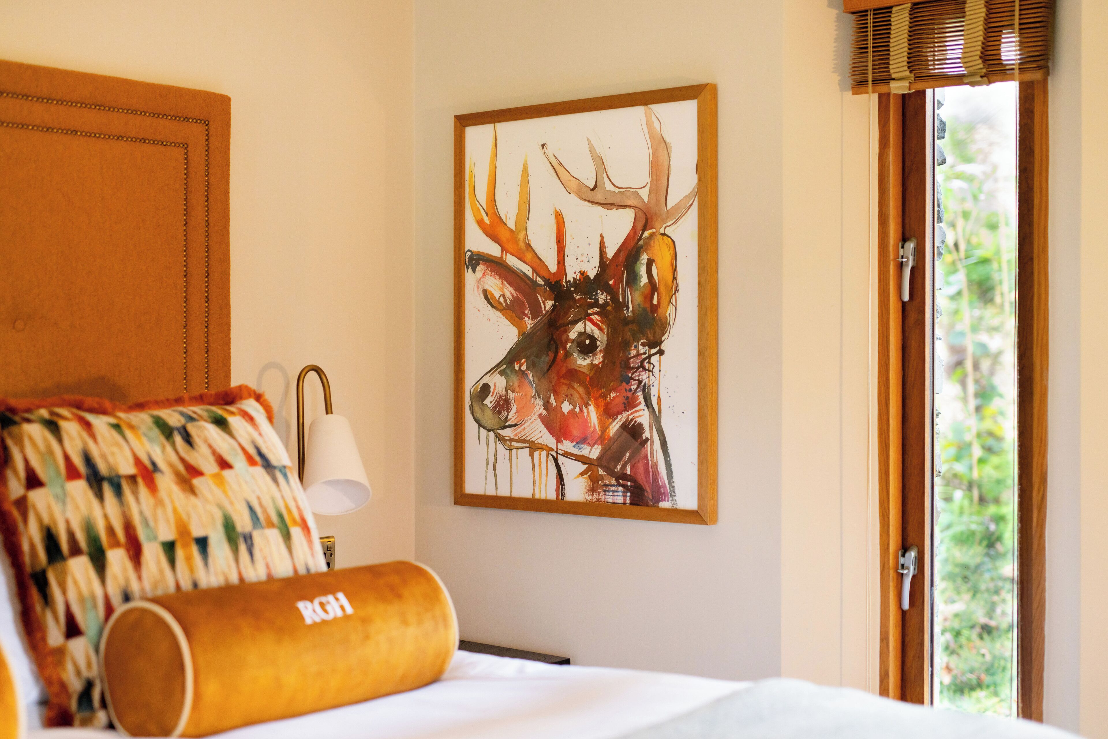 Een hotelkamer met een bed, een kleurrijk quilt, een schilderij van een hert en een raam met uitzicht op groen.