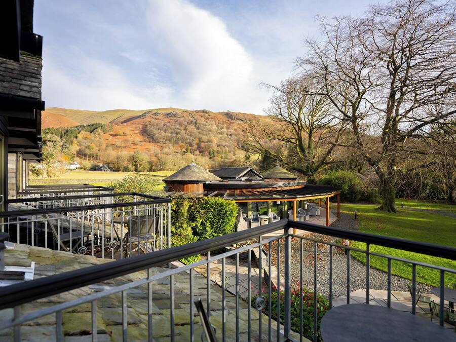 A balcony with a stone balustrade overlooking a landscaped garden, a wooden gazebo, and a view of a hillside.