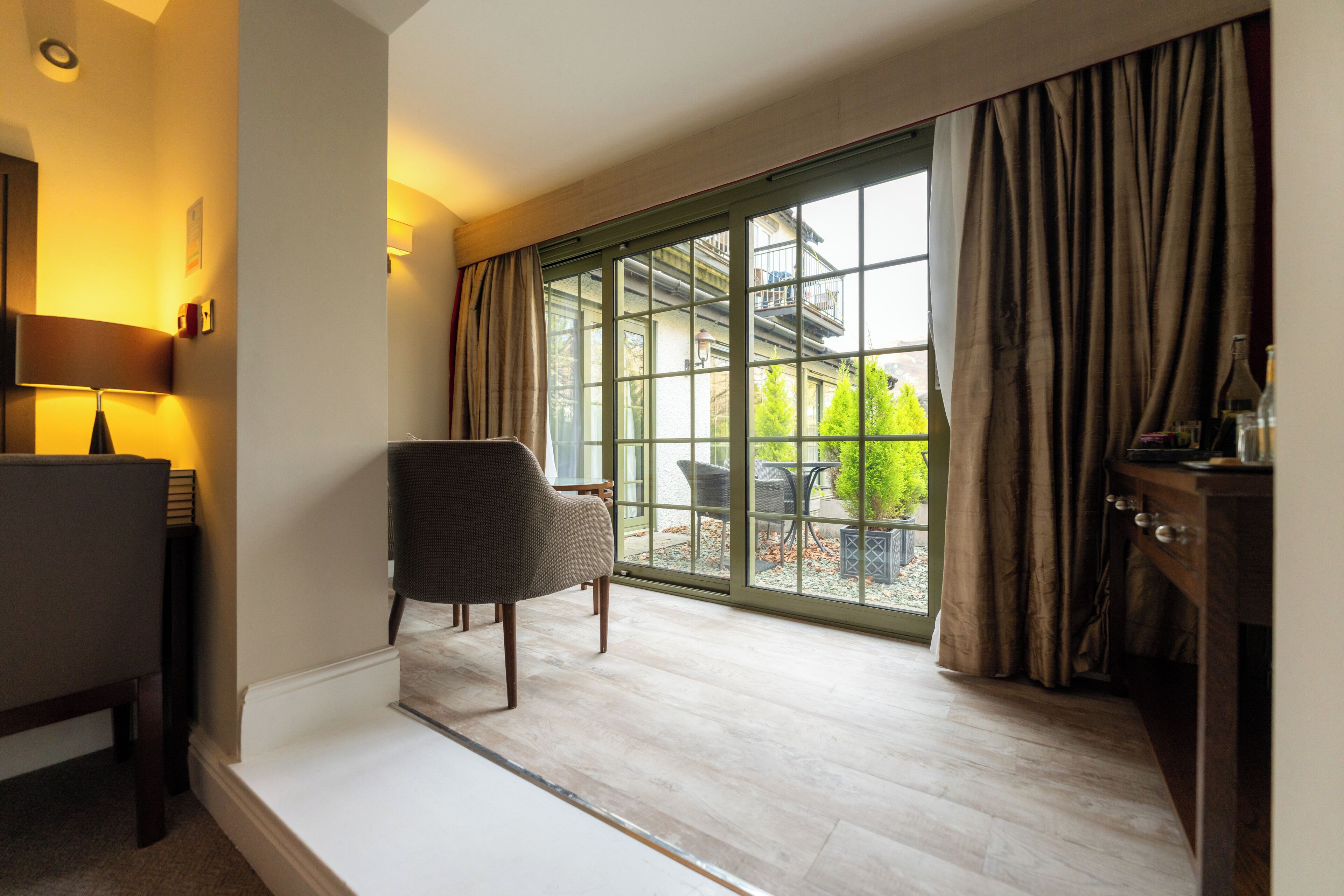 A room with a large sliding glass door leading to an outdoor area, a chair, a small table, and a lamp.