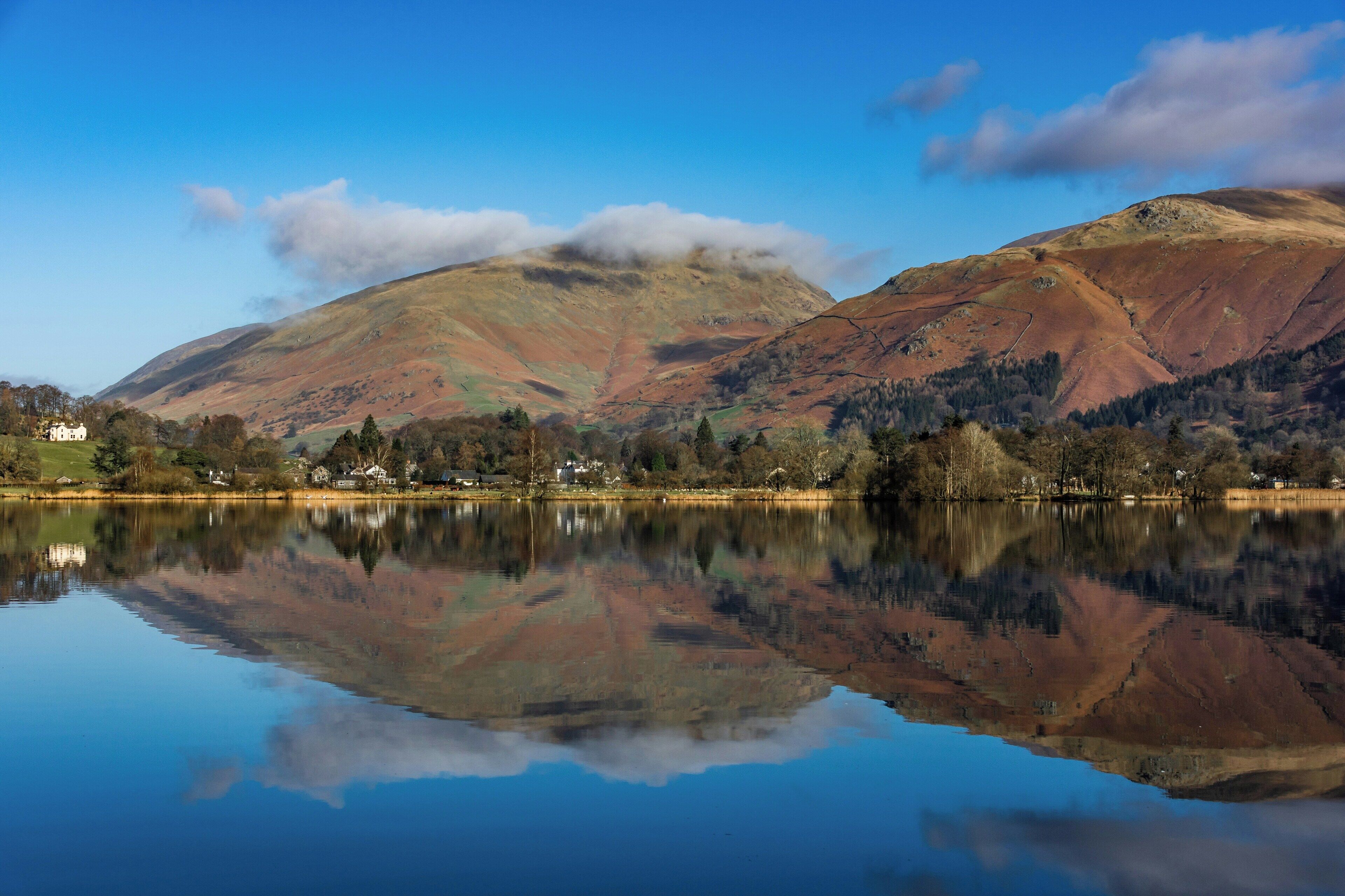 A calm lake reflecting mountains and a small village.