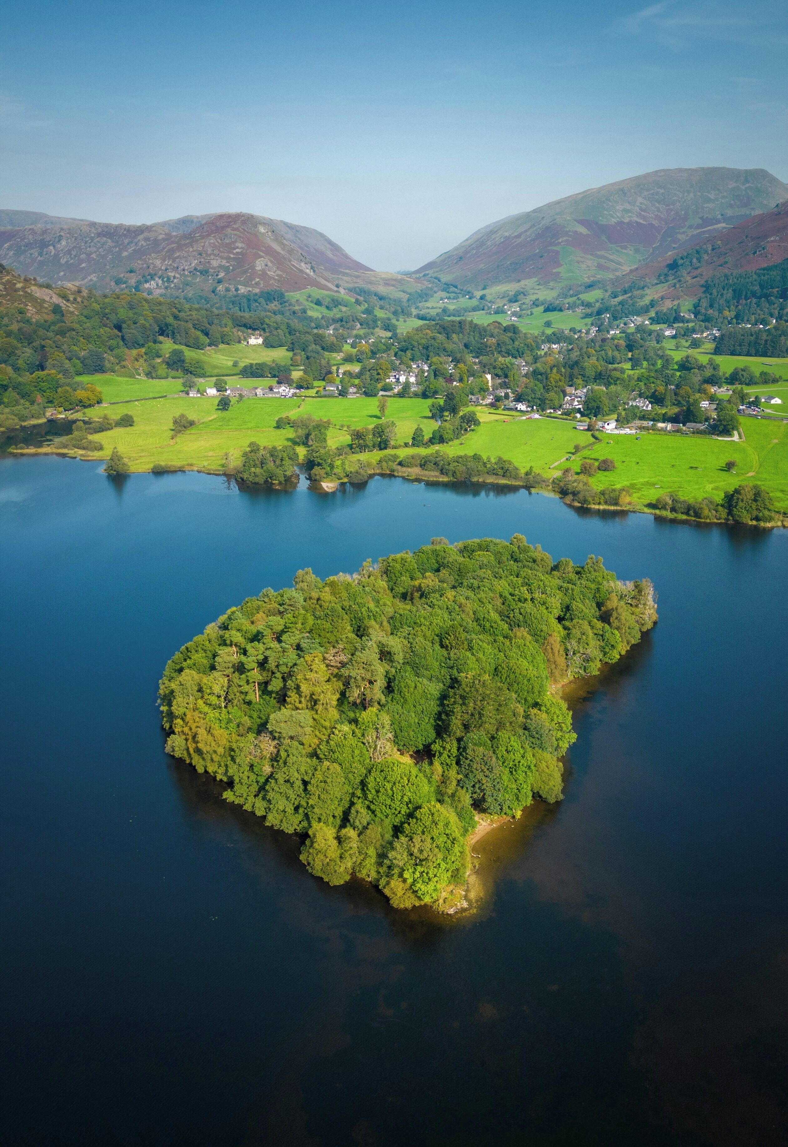An aerial view of a lake surrounded by green hills and a small island with dense trees.