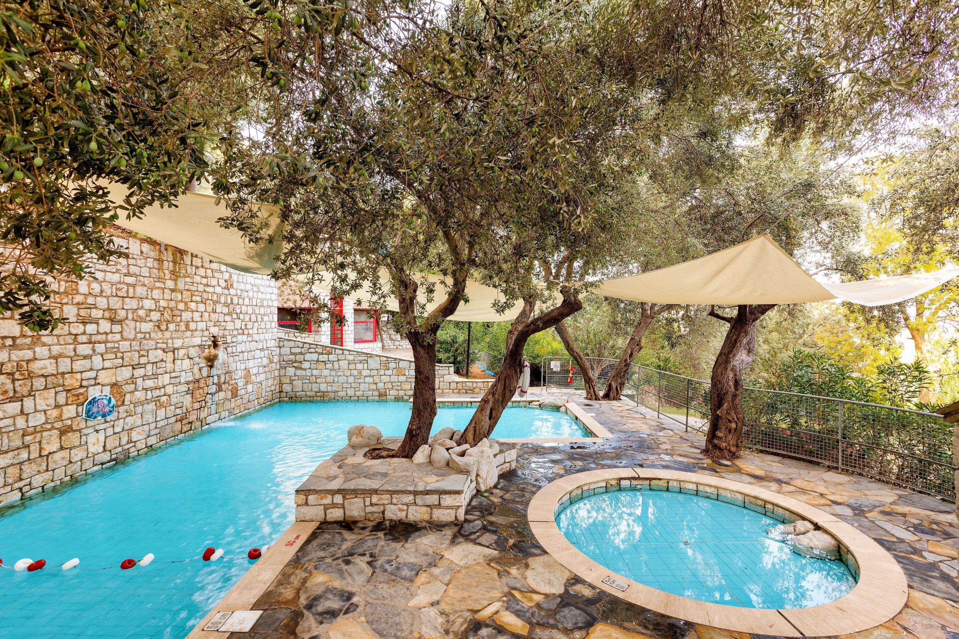 Un espace piscine agrémenté de murs en pierre et d’arbres, le tout entouré d’une clôture.