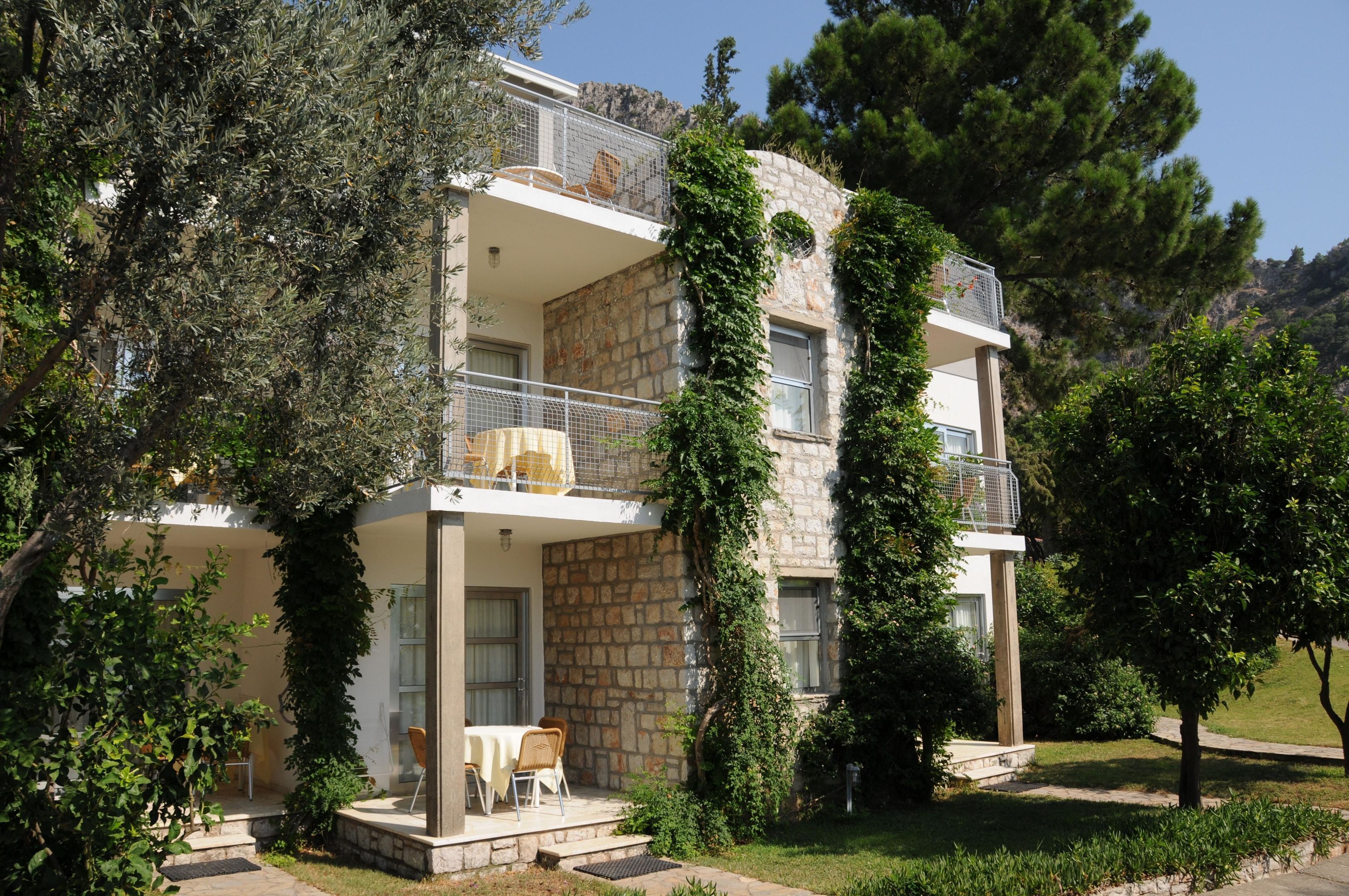 Un bâtiment en pierre de deux étages, doté d’un balcon et entouré de verdure et d’arbres.