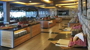 Zona de buffet con varias estaciones de comida, arreglos de asientos y una pared de piedra con un cuadro colgado.