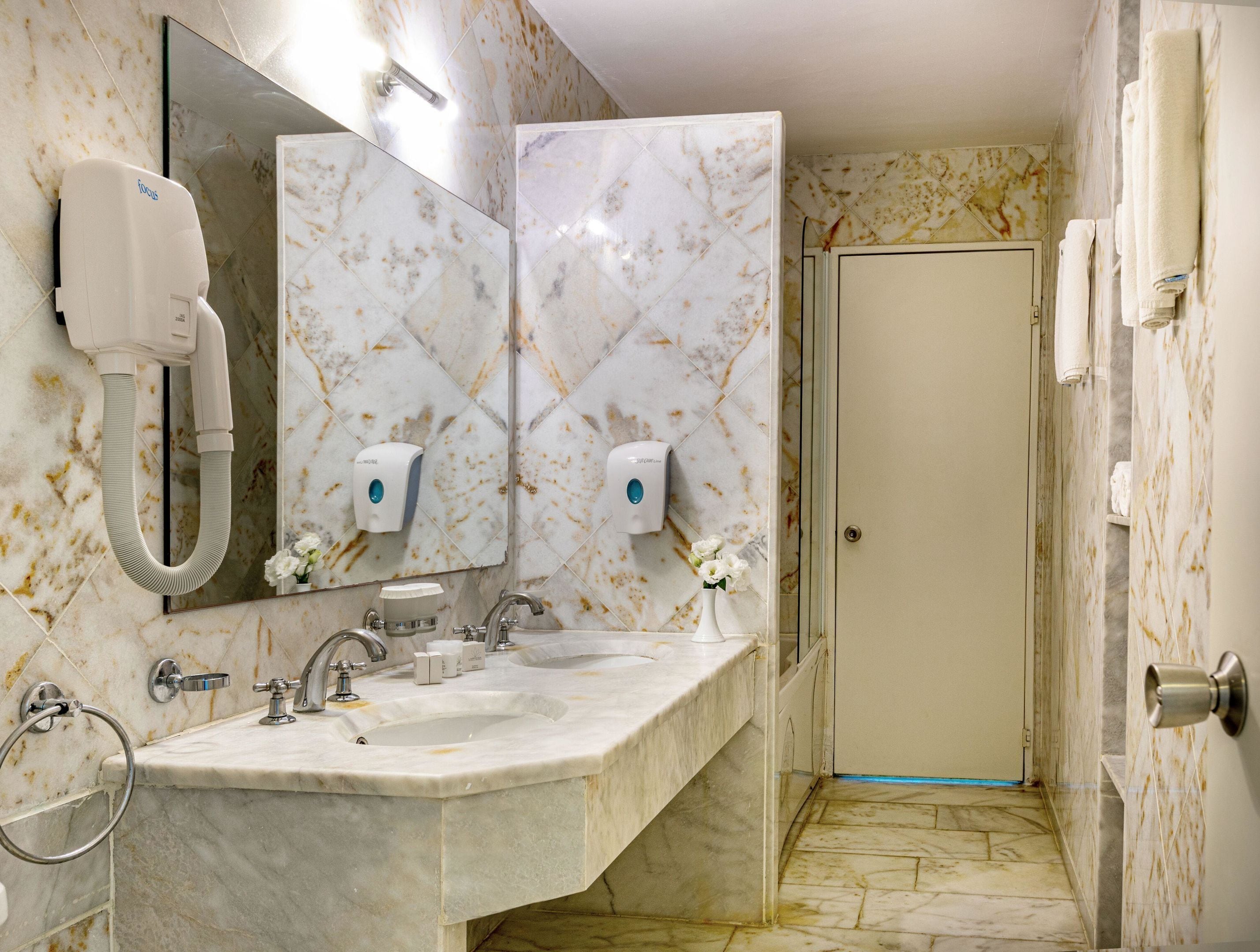 A bathroom with a marble sink, two hand dryers, a mirror, and a door.