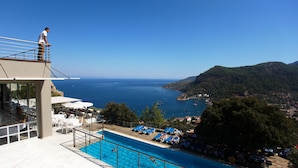 Zona de piscina con vista al mar, sillas de descanso y una persona parada en un balcón.