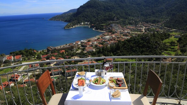 Mesa en balcón con comida, con vista a un pueblo costero y al mar.