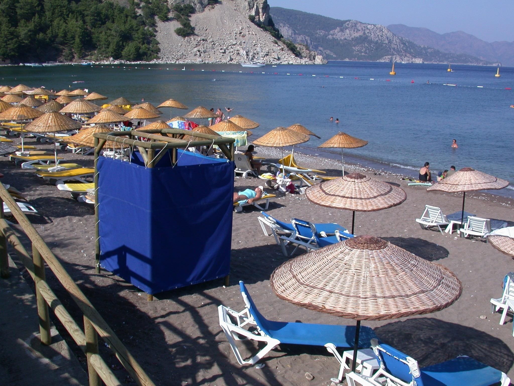 A beach with umbrellas, lounge chairs, and a rocky coastline.