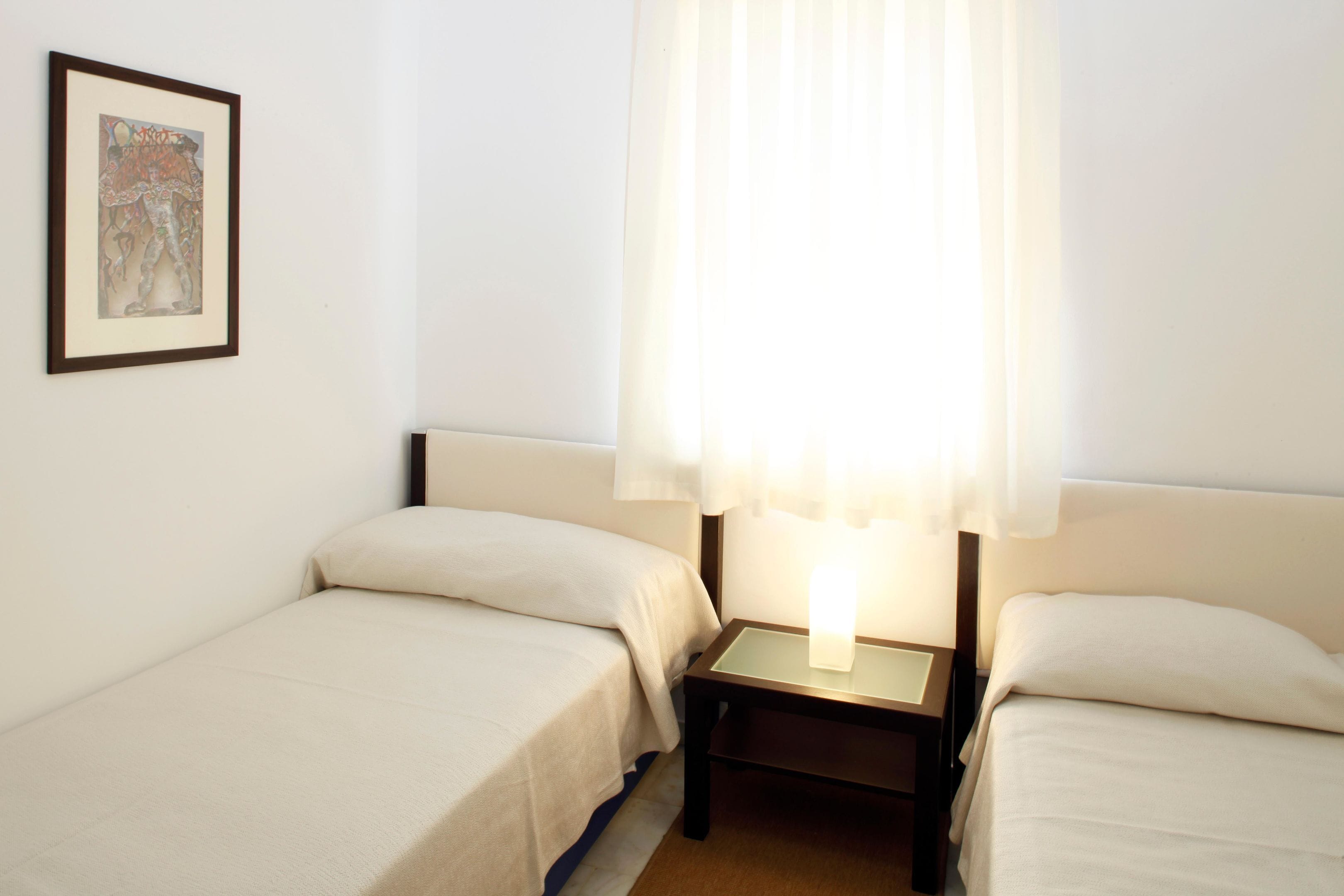 A hotel room with two single beds, a nightstand with a lamp, and a framed picture on the wall.