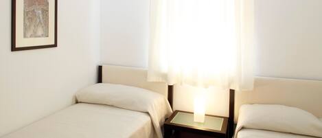 A hotel room with two single beds, a nightstand with a lamp, and a framed picture on the wall.