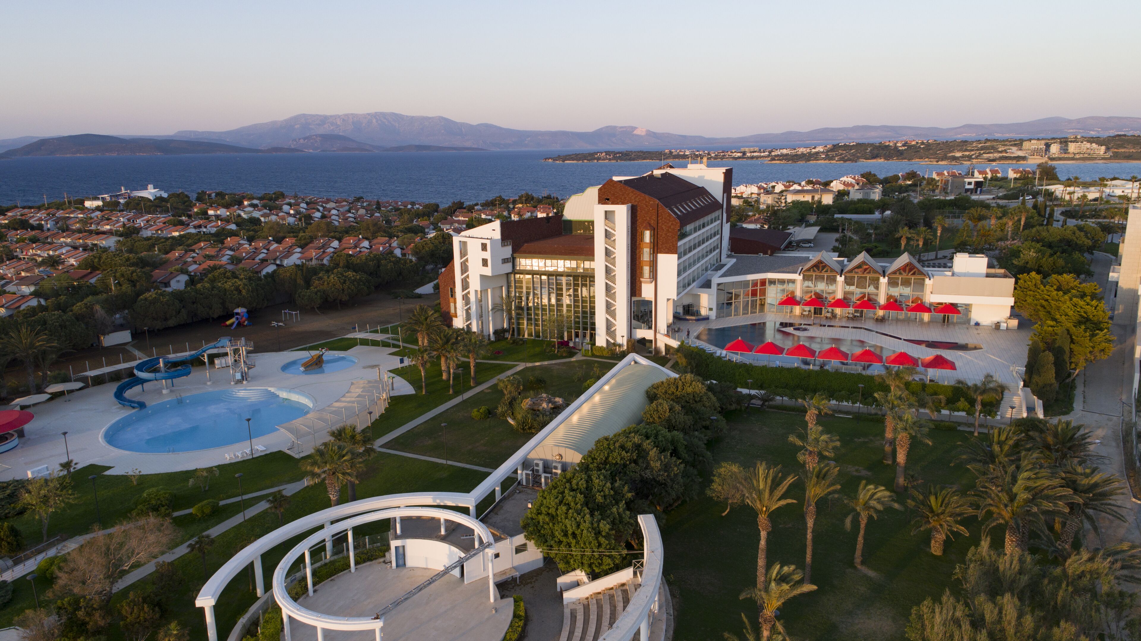 A resort with a swimming pool, a landscaped area with palm trees, and a view of the sea.
