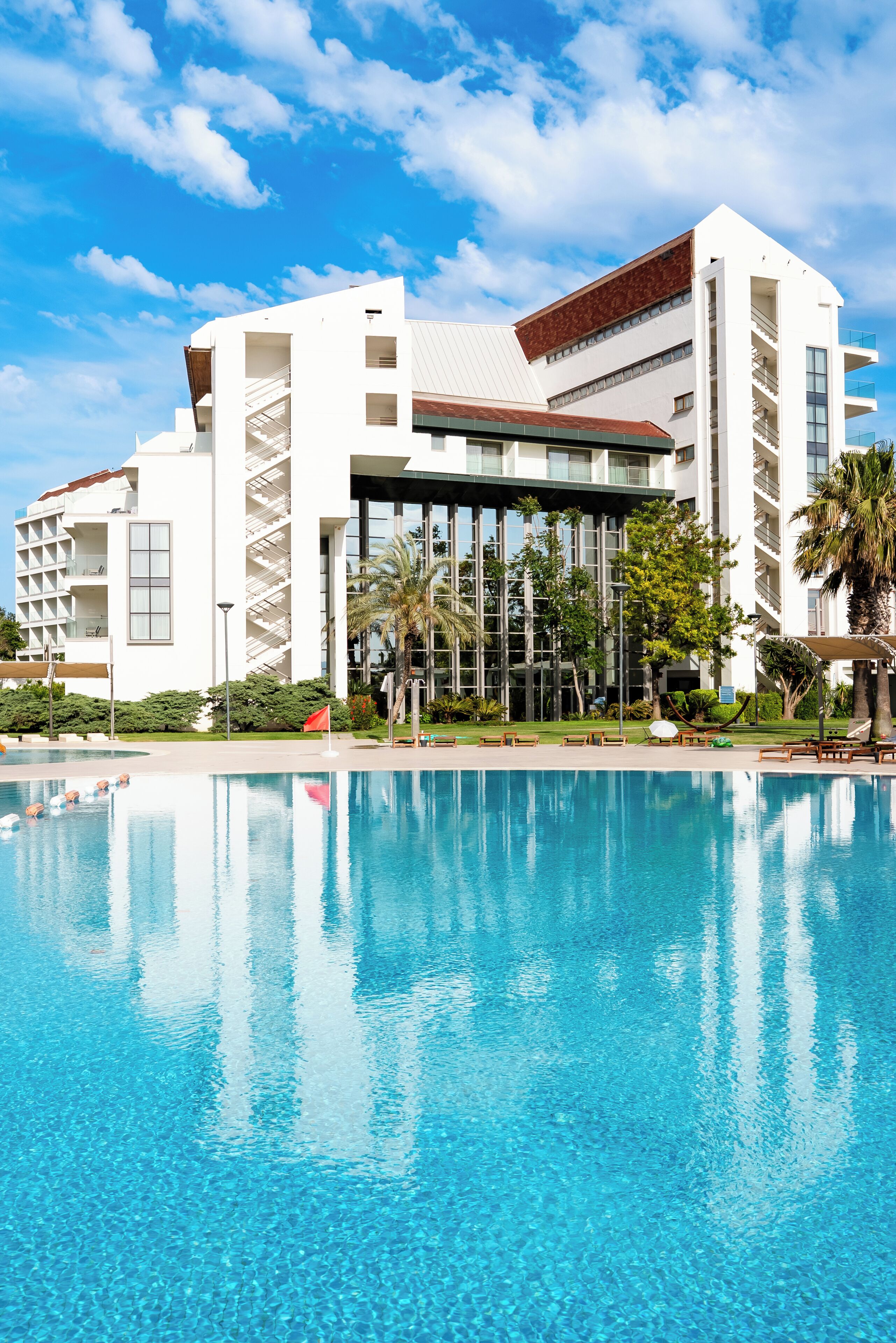 A modern hotel with a large pool, multiple balconies, and a clear blue sky.