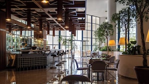 A modern restaurant interior with a bar area, seating, and large windows allowing natural light. - Grand Hotel Ontur (Cesme)