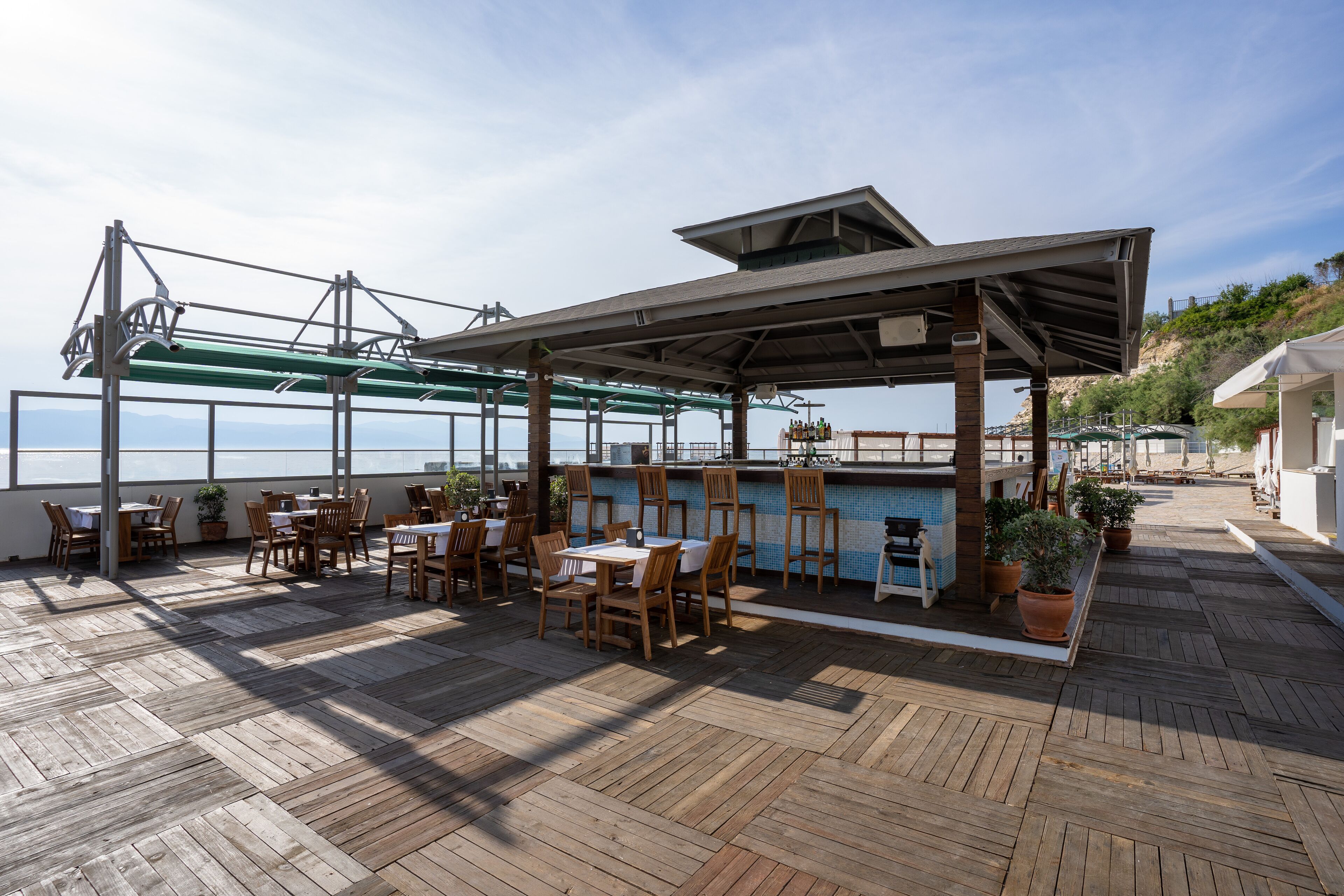Un espace extérieur aménagé pour les repas, avec un sol en bois, des tables, des chaises et des plantes en pot.