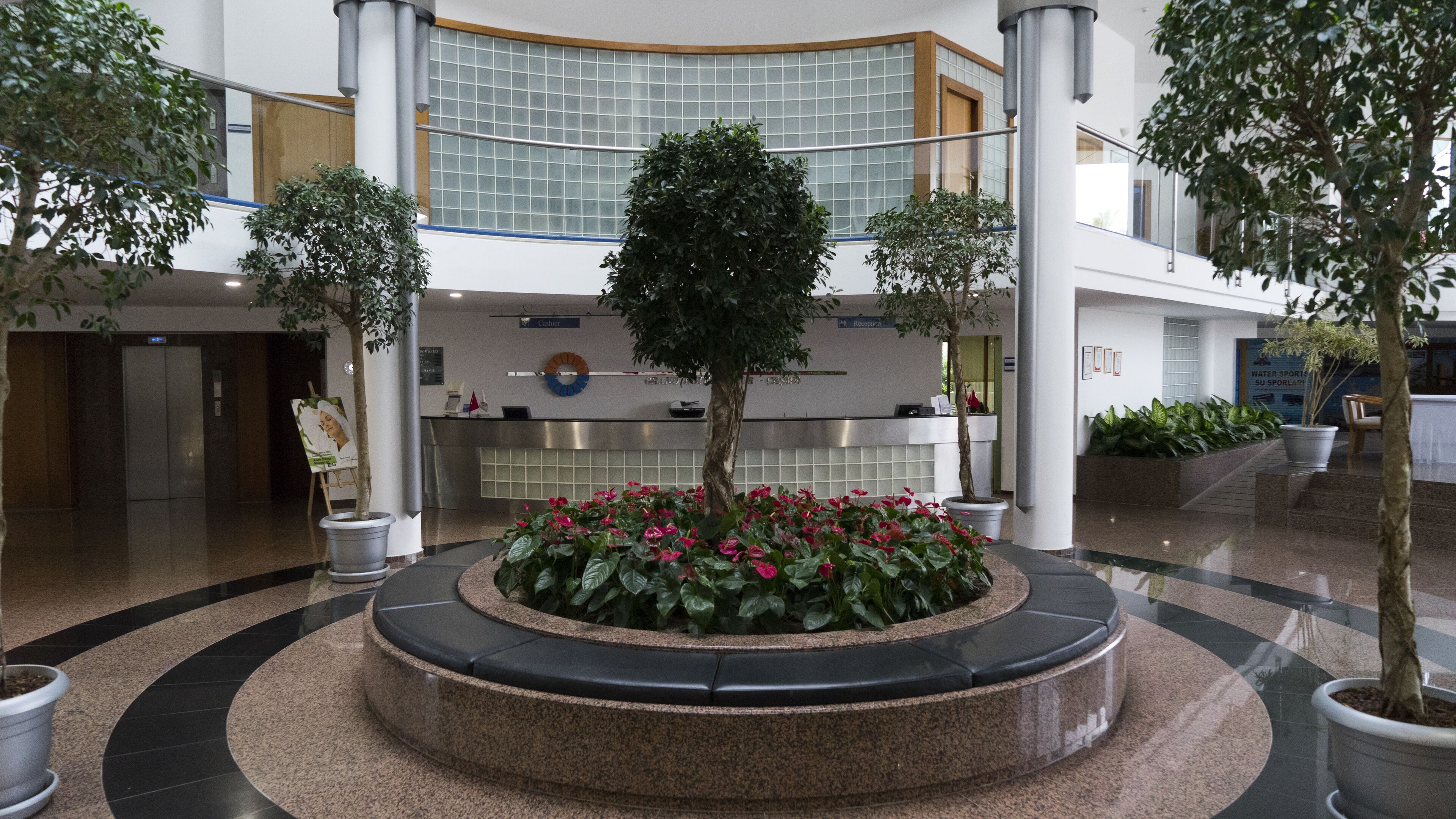 A lobby with a central circular planter with flowers, a reception desk, and a glass wall in the background.