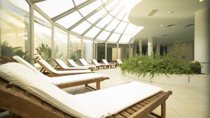 A sunlit indoor relaxation area with wooden loungers and a glass ceiling. - Grand Hotel Ontur (Cesme)