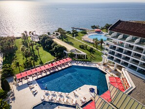 Un resort con una piscina grande, sillones de sol y vista al océano.
