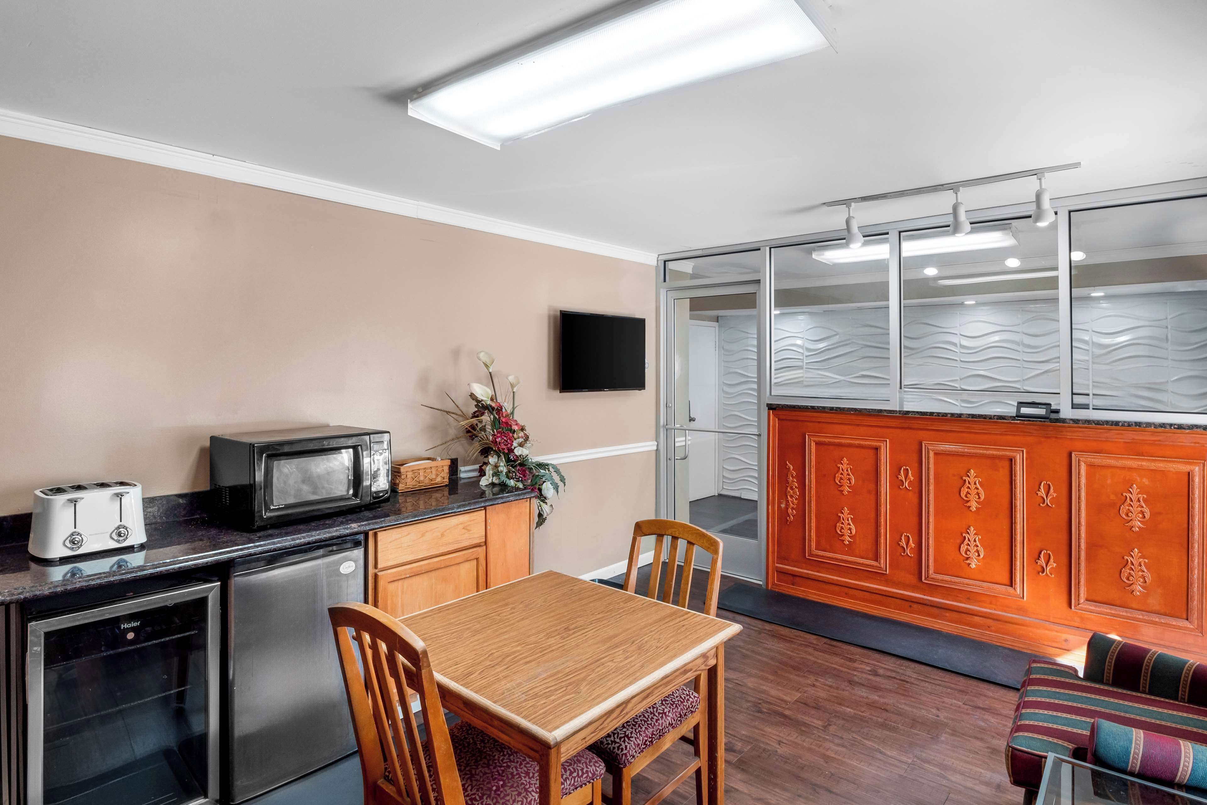 A compact kitchen with a toaster, microwave, and refrigerator. There is a wooden dining table with chairs and a sofa in the living area.