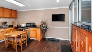 A compact kitchen with wooden cabinets, a dining table, and a flat-screen TV mounted on the wall.