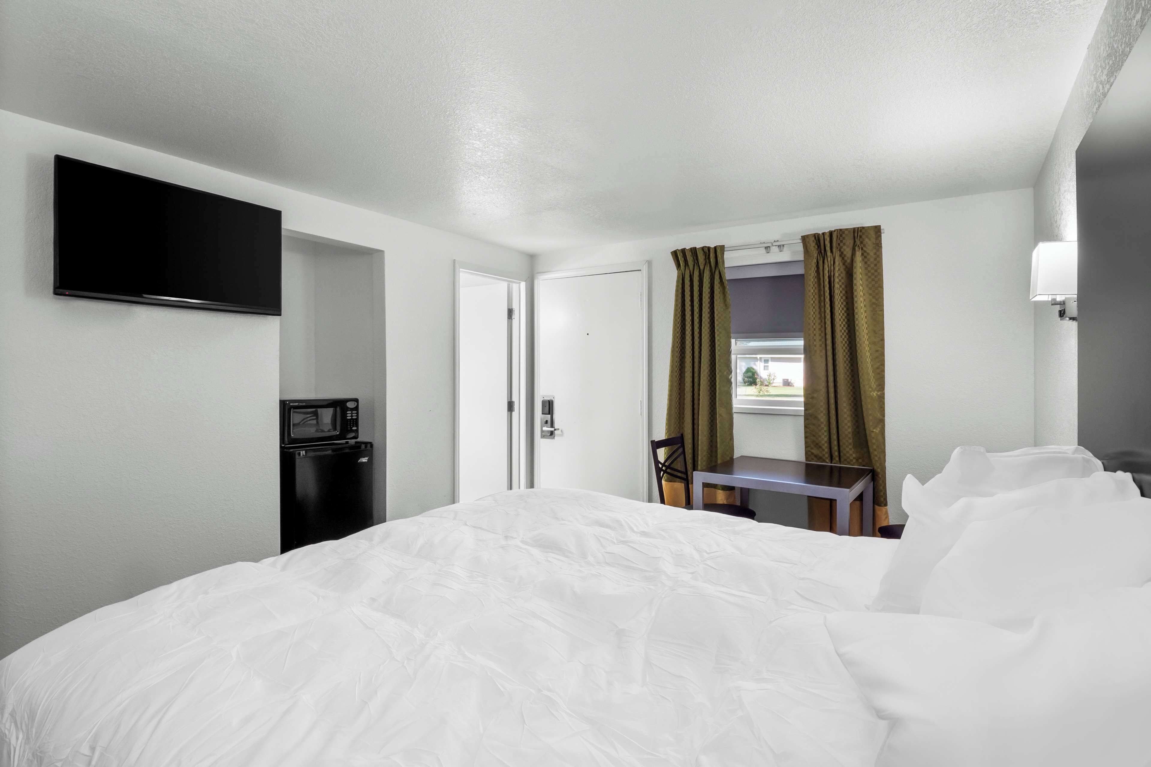 Hotelkamer met een groot bed, een flatscreen televisie aan de muur, een magnetron, een klein tafeltje met een stoel, en een raam met gordijnen.